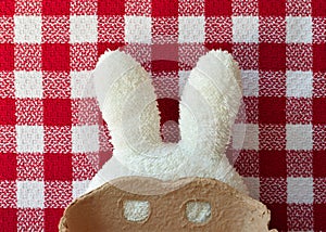 White toweling bunny ears with a carboard mask. Red square tablecloth in the background