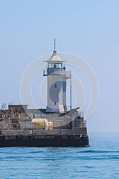 The white tower of the lighthouse and the old cannon at the entrance to the sea port of Yalta. In the background the