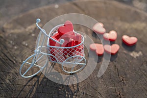 White toy bike carrying red wooden hearts. Red wood hearts fall on the wooden floor. Heart-shaped toys convey to Valentine`s Day