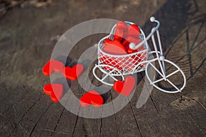 White toy bike carrying red wooden hearts. Red wood hearts fall on the wooden floor. Heart-shaped toys convey to Valentine`s Day