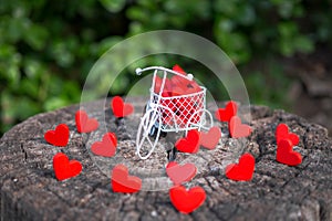 White toy bike carrying red wooden hearts. Red wood hearts fall on the wooden floor. Heart-shaped toys convey to Valentine`s Day