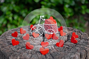 White toy bike carrying red wooden hearts. Red wood hearts fall on the wooden floor. Heart-shaped toys convey to Valentine`s Day