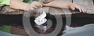 White toy boat in child hand at a pier in a pond in summer