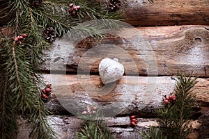 White toy-heart on wooden planks with spruce branches and red berries all around.