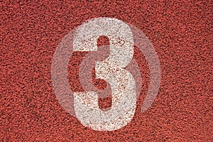 White track number on red rubber racetrack, texture of running racetracks in small outdoor stadium