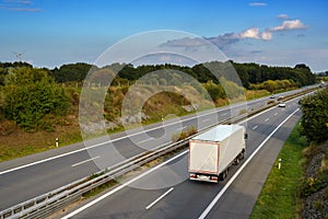 White truck is driving on the highway through the country landscape under a blue sky with clouds, transport and environment