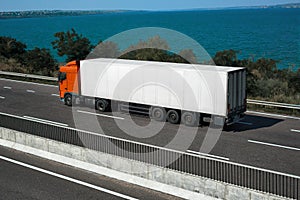 White truck is going up the road near the sea. Cargo transportation concept