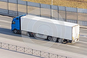 White truck with gray awning trailer rides on a city highway, side aerial view