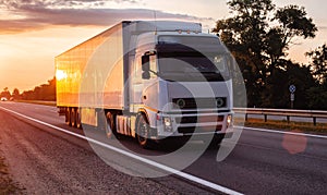 White truck with refrigerated semitrailer transport frozen food on the highway in the evening against the backdrop of