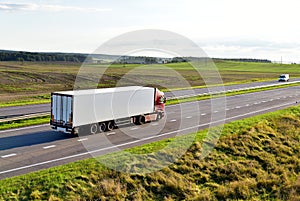 White truck with semi-trailer driving along highway on the sunset background. Goods delivery by roads. Services and Transport