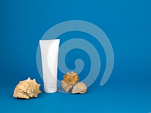 White tube and whelk seashells on blue background. Mockup plastic tube for sunscreen, nourishing or moisturizing cream