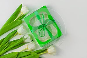 White tulip flowers and green gift box on light background flat lay. Bouquet greeting card. Website banner top view