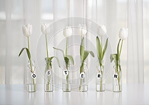 White tulips in bottles with Easter decoration in the form of eggs on a white table