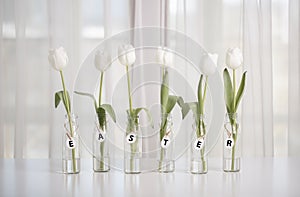 White tulips in bottles with Easter decoration in the form of eggs on a white table