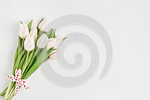 White tulips bouquet decorated with hearts ribbon on white wooden background. Copy space. Valentines Day concept