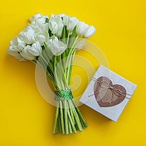 White tulips and gift box on bright yellow background. Spring concept.