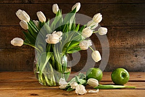 White tulips in glass vase on rustic wood