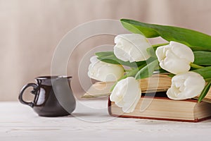 White tulips, old books, a Cup of coffee in the distance on a beige background. Morning, spring, reading, coffee break