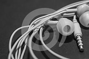 White twisted wired headphones on a monochromatic black surface, close-up. Headset for a mobile phone. Music.