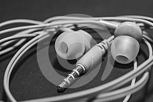 White twisted wired headphones on a monochromatic black surface, close-up. Headset for a mobile phone. Music.