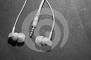 White twisted wired headphones on a monochromatic black surface, close-up. Headset for a mobile phone. Music.