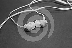 White twisted wired headphones on a monochromatic black surface, close-up. Headset for a mobile phone. Music