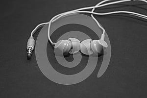 White twisted wired headphones on a monochromatic black surface, close-up. Headset for a mobile phone. Music