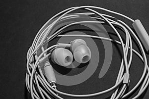 White twisted wired headphones on a monochromatic black surface, close-up. Headset for a mobile phone. Music