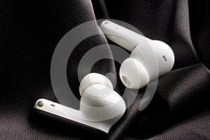 White TWS headphones in black silk interior. The concept of the noise reduction function in modern audio equipment and tws