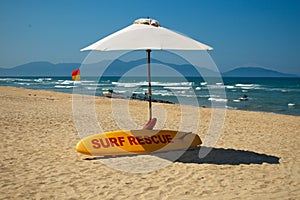 White umbrella beach and yellow surf board on a sandy beach with blue sea background