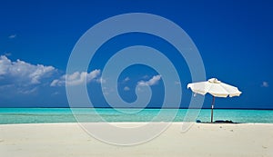 White umbrella on idyllic tropical sand beach. White beach umbrella and blue sky. Sun and umbrella on the beach. Summer beach