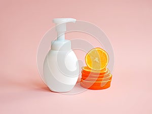 White unbranded bottle with pump and orange slices  on light pink background. Blank container for lotion, cream, sunscreen,