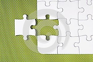 White unfinished jigsaw puzzle on green background, with one missing piece