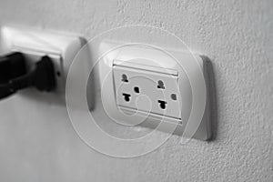 White universal electricity sockets plug on a white wall.