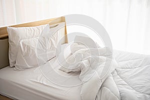 White unmade bed in the morning with sunshine with white curtain background in elegant home. Interior design and luxury furniture