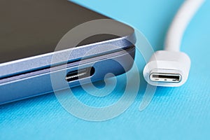 White USB type-c plug and its corresponding port on a modern laptop - ultrabook on a blue background. Modern information