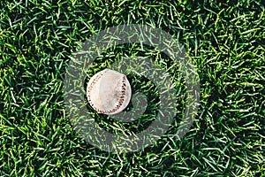 A white used baseball on the fresh green grass