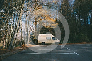 White van parked in the parking lot surrounded by beautiful green trees