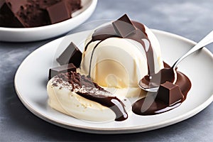 White vanilla ice cream with chocolate topping and brown dark chocolate pieces on a white plate. Delicious sweet dessert