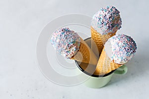 White vanilla ice cream scoop in waffle cone with sprinkles in cup on light grey background