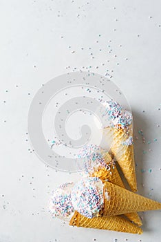 White vanilla ice cream scoop in waffle cone with sprinkles on light grey background