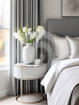 White vase with flowers on round nightstand near bed. Art deco style interior design of modern bedroom. Created with generative AI