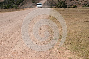 White vehicle driving unsealed, dirt road with clouds of dust