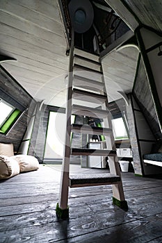 White vertical wooden stairs to the second floor from living room of summer house. Pyramid shape bungalow from inside. Floor walls