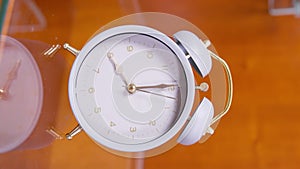 White vintage alarm clock with a large bells stands on a glass bedside table, showing how the time is approaching 8