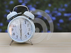 white vintage alarm clock showing 6 o clock on the table in the garden with purple flowers background