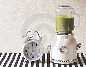 White vintage blender or smoothie maker  with white vintage alarm clock 7 o`sclock  on  black and white stripe table cloth and