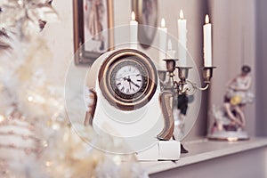 White vintage clock at the burning candles background.