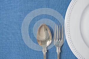 White Vintage Empty Plate Half Circle Silver Fork Spoon on Light Blue Linen Fabric. Minimalist Japanese Style Table Setting