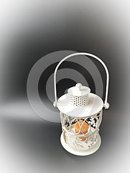 White vintage lantern with an orange candle on black.